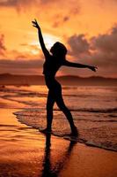 silhouette of a very slender ballerina doing ballet practice alone on the seashore with waves crashing at her photo