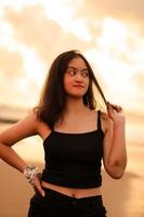 an Asian woman with black clothes and long black hair standing on the beach sand with a flat expression while on vacation photo