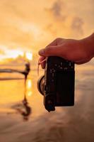 A Camera with hands photographs a Balinese woman doing a gymnastic movement on a black shirt near the beach photo