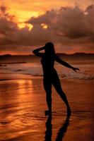 silhouette of an Asian woman dancing ballet with great flexibility and a view of the waves behind her photo