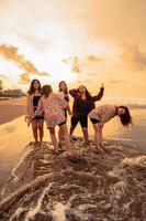 un grupo de indonesio mujer disfrutar el playa felizmente cuando ellos reunirse su amigos a el fiesta momento foto