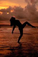 silueta de un asiático mujer jugando en el agua en el playa con fuerte olas estrellarse foto