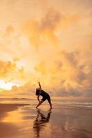 an Asian woman is doing gymnastic movements on the beach with clouds behind her and the waves crashing photo