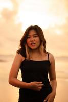 An Asian woman poses with a dirty and angry expression when wearing a black dress on the beach photo