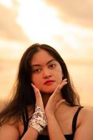 An Asian woman with long black hair poses with her hands while enjoying the view of the beach photo