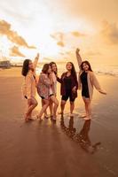 un grupo de asiático mujer en camisas posando felizmente mientras visitando un hermosa playa foto