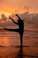 An Asian woman in the form of a silhouette doing ballet movements very agile on the beach photo