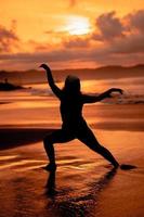 silueta imagen de un asiático mujer haciendo ballet movimientos muy flexiblemente en el playa foto