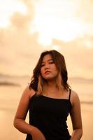 An Asian woman poses with a dirty and angry expression when wearing a black dress on the beach photo