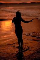 silueta de un asiático mujer jugando en el agua en el playa con fuerte olas estrellarse foto