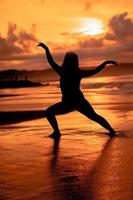 silueta imagen de un asiático mujer haciendo ballet movimientos muy flexiblemente en el playa foto