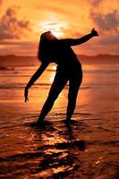 el silueta de un indonesio adolescente bailando muy flexiblemente con el estrellarse olas en el playa foto