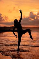 A Balinese woman in the form of a silhouette performs ballet movements very deftly and flexibly on the beach with the waves crashing photo