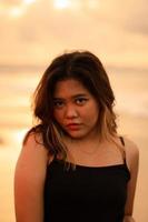 A Portrait of an Asian woman in a black dress doing a sexy pose while enjoying the view near the beach photo