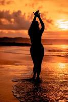 the silhouette of an Asian teenager with a tall body is dancing ballet on the waves on the beach photo