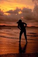 un asiático mujer quien es jugando y bailando en el playa con fuerte olas foto