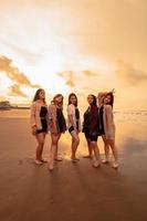 un grupo de asiático mujer en camisas posando felizmente mientras visitando un hermosa playa foto