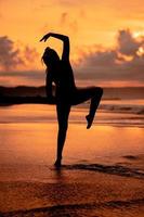 un asiático mujer en el formar de un silueta haciendo ballet movimientos muy ágil en el playa foto