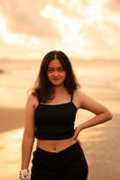an Asian teenage girl in a black shirt looks very happy as can be seen from her expression while on vacation by the beach photo