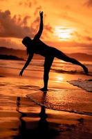 silhouette of an Asian woman dancing ballet with great flexibility and a view of the waves behind her photo