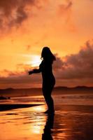 an Asian woman in silhouette is doing a very beautiful dance on the beach with the waves crashing photo