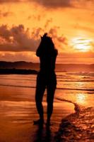 the silhouette of an Asian teenager with a tall body is dancing ballet on the waves on the beach photo