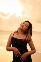 An Asian woman with brown hair and black clothes makes sexy poses very skillfully while enjoying the beach photo