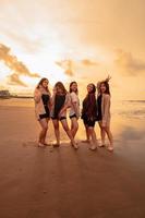 un grupo de asiático mujer en camisas posando felizmente mientras visitando un hermosa playa foto