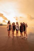 un grupo de asiático mujer en camisas posando felizmente mientras visitando un hermosa playa foto