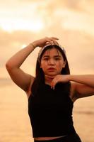 a glamorous Asian woman in black clothes and a white bandana standing in front of the waves on the beach photo