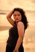 an Asian woman posing with her hands raised and touching her black hair passionately on the beach photo