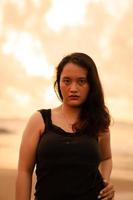 portrait image of an Asian woman with black hair and an angry expression standing on the beach in her black clothes photo