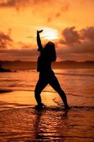 silueta imagen de un asiático mujer haciendo ballet movimientos muy flexiblemente en el playa foto