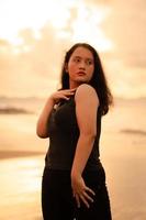 an Asian woman posing with her hands raised and touching her black hair passionately on the beach photo