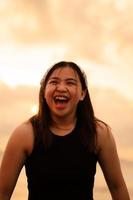 an Asian teenager wearing a white bandanna and a black shirt with a goofy and happy expression on the beach photo