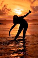 the silhouette of an Indonesian teenager dancing very flexibly with the crashing waves on the beach photo