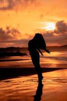 un asiático mujer en silueta es haciendo un muy hermosa danza en el playa con el olas estrellarse foto