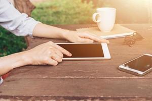 Hand woman using tablet on table in garden at coffee shop with vintage toned. photo