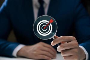 Businessman showing magnifying glass focusing on goal icon, corporate development and global business leadership, success, strategy, prospects, sustainable goals. photo