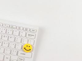 flat lay of  yellow circle smiling face on white computer keyboard on white  background. photo