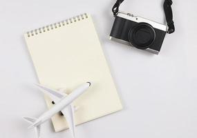 flat lay of blank page opened notebook, airplane model  and camera on white  background with copy space. Travel, photo and memory concept.