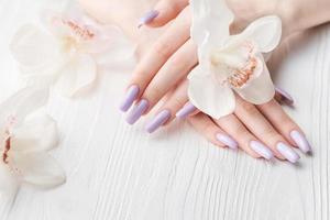 manos de niña con delicada manicura púrpura y flores de orquídeas foto
