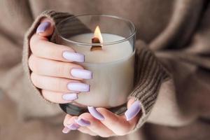 las manos de una joven con una hermosa manicura violeta claro sostienen una vela foto