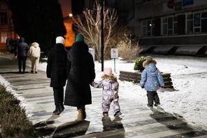 Back of family walk through the night city in the winter. Mother and three children in evening. photo