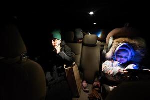 At the back seat of car mother with children look at phone in night driving. photo