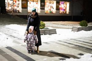 Mother and baby girl in the night city at winter. Mom with daughter in evening. photo