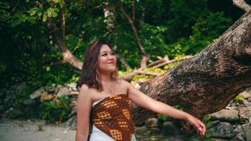 a woman with blonde hair holding a tree trunk while walking on an island for vacation video