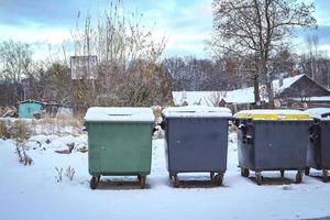 Green and grey plastic dumpster waste and garbage containers on wheels on thin snow in winter season photo
