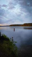 Man in the water knee deep in evening dusk with heavy clouds and visible forest on the other side photo