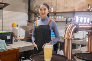 retrato de asiático barman niña mano a cerveza grifo torrencial , camarera o personal servir y artesanía, Barril cerveza en vaso servicio en un restaurante o pub cerveza foto
